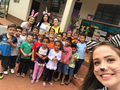 Crianças e integrantes do Grêmio Estudantil posam para a foto, em frente à escola. Em primeiro plano está o rosto de uma aluna do IFFar, com maquiagem de cachorro, alusiva ao dia das crianças.